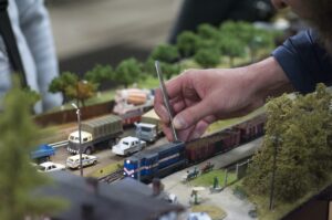 鉄道模型のジオラマ作りをする男性の手とピンセットで調整される線路上の列車